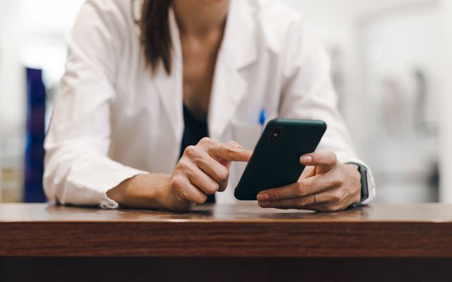 Woman in healthcare uniform using smartphone, representing digital employee engagement and HR-Software.