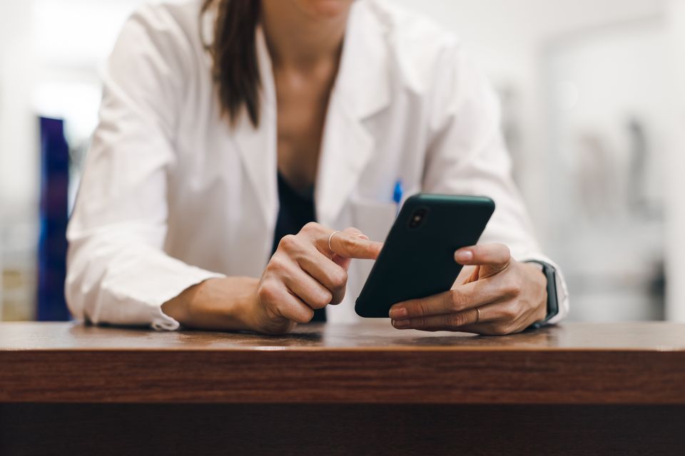 Woman in healthcare uniform using smartphone, representing digital employee engagement and HR-Software.