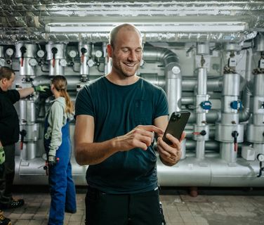 Industrial workers in a plant; one uses a smartphone, highlighting digital employee empowerment.