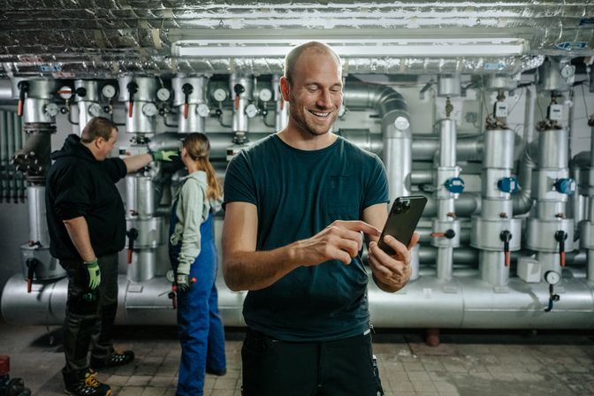 Industrial workers in a plant; one uses a smartphone, highlighting digital employee empowerment.