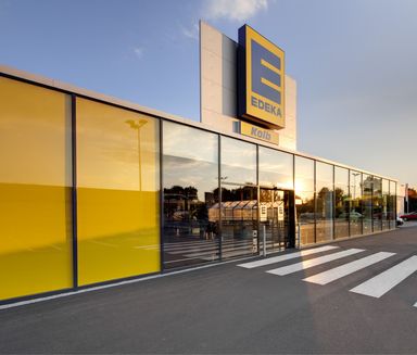 Modern EDEKA supermarket entrance with glass facade, yellow panels, and EDEKA Kolb signage.
