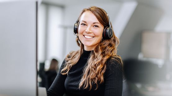 Smiling woman with headset at desk, representing service and support for frontline employees.