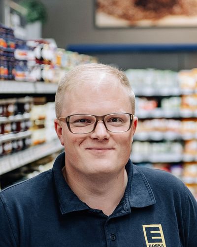 Smiling EDEKA-Mitarbeiter im Supermarktregal, freundliche Atmosphäre, Kundenservice.