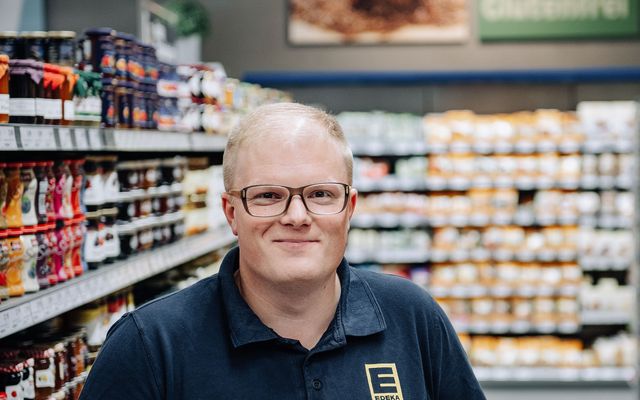Smiling EDEKA-Mitarbeiter im Supermarktregal, freundliche Atmosphäre, Kundenservice.