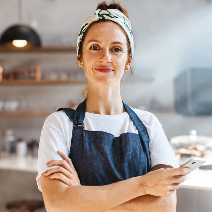 Smiling woman in an apron holding a phone in a cafe setting.