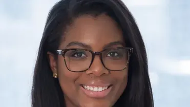 Professional woman with glasses smiling, wearing a white blouse, neutral background.