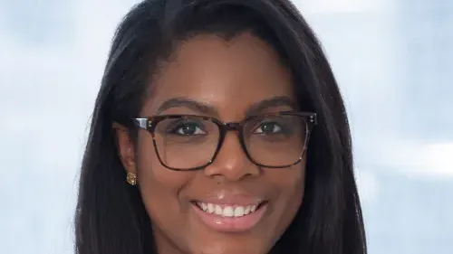 Professional woman with glasses smiling, wearing a white blouse, neutral background.