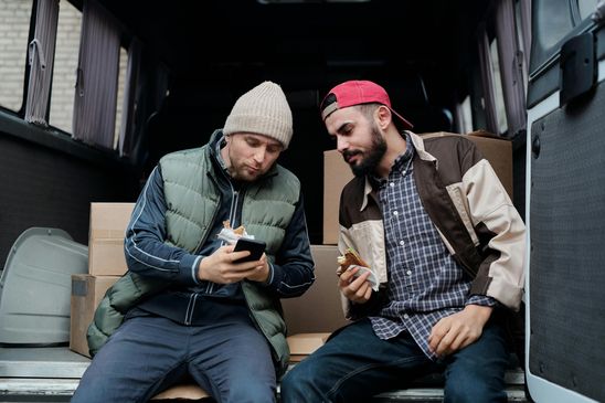 Two men sitting in a van, looking at a smartphone.