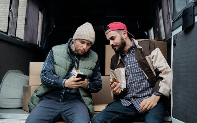 Two men sitting in a van, looking at a smartphone.
