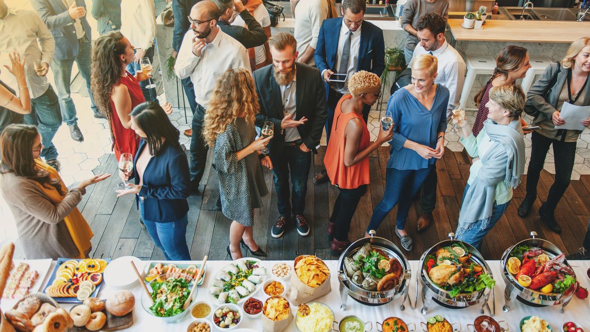 People networking and socializing at a dinner event with a buffet table of food and drinks.