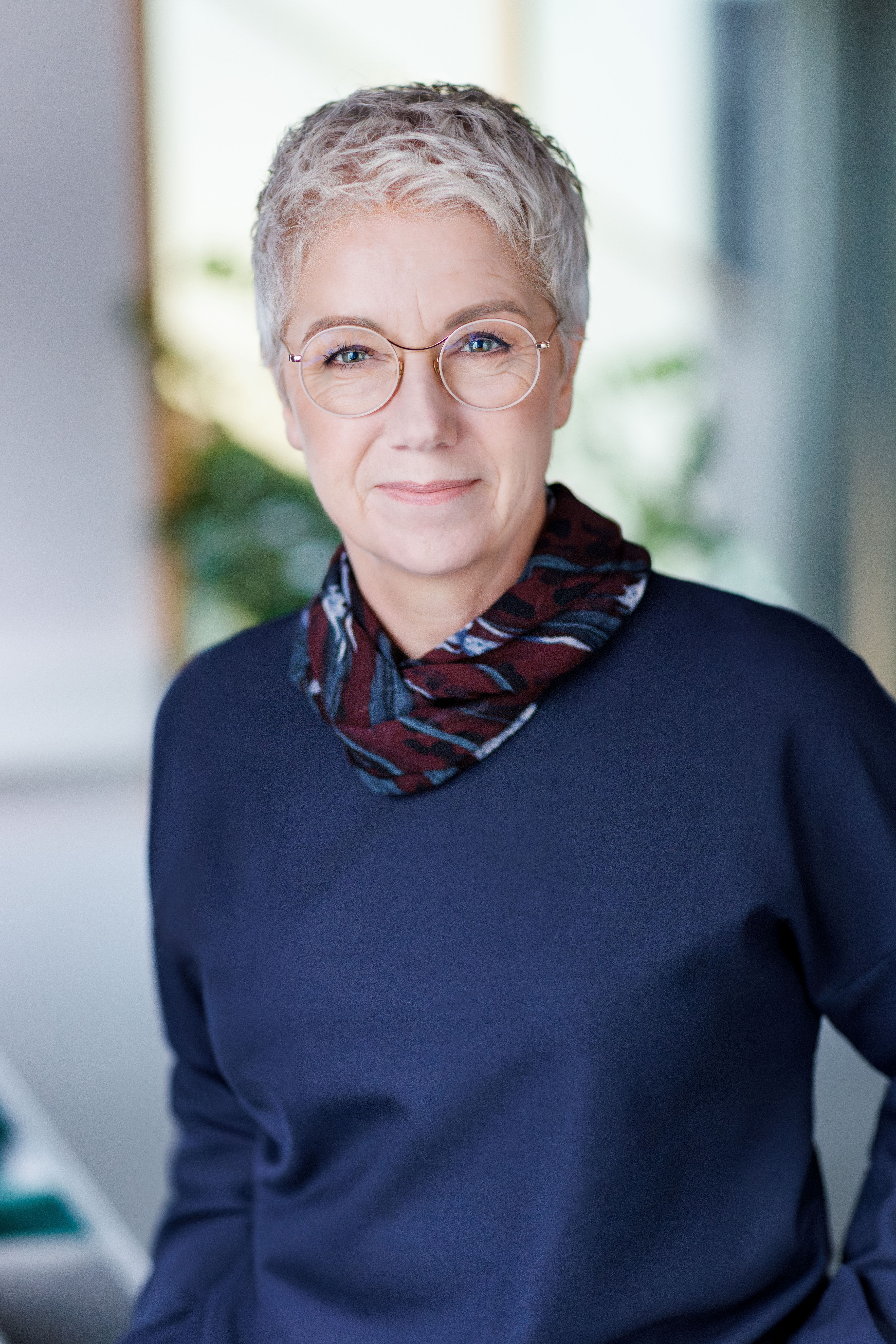 Portrait of a person with short hair and glasses, wearing a scarf.