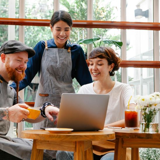 Three cafe employees smiling and looking at a laptop.