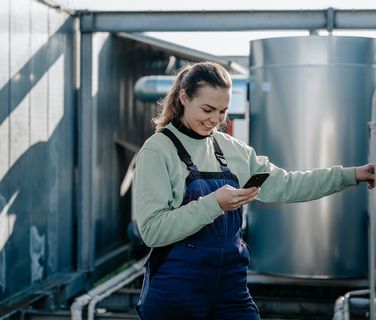 Woman in industrial plant using smartphone, symbolizing Employee App, Mitarbeiterplattform, HR-Software.