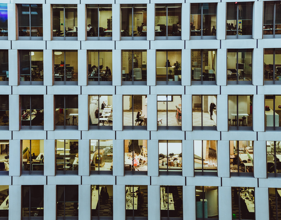 Office building windows showing multiple workspaces and employees; no visible software interface.