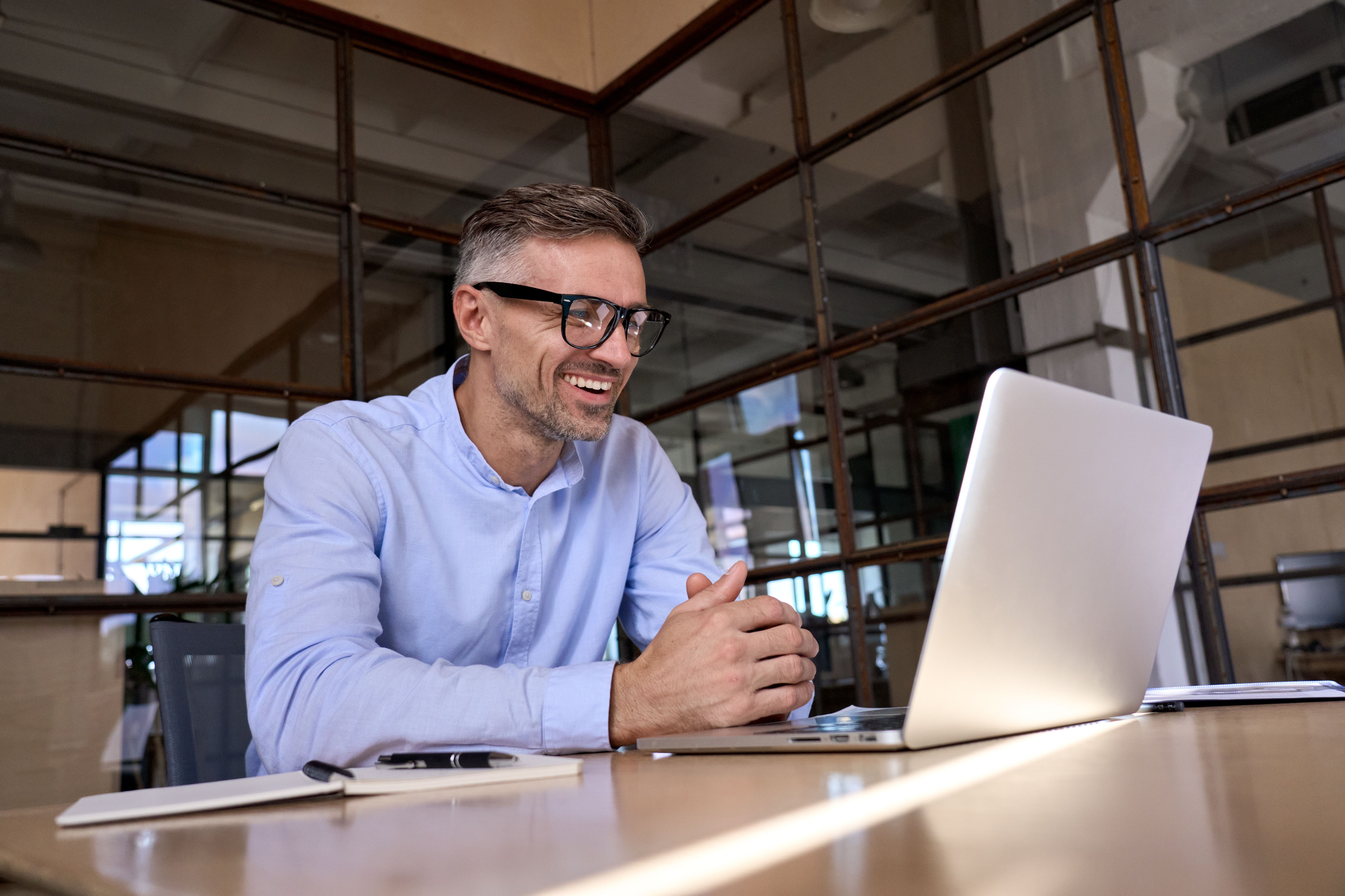 Smiling man sitting at desk with laptop in modern office environment.