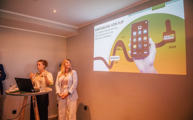 Two people presenting a slide titled Einführung von Flip with a mobile app image.