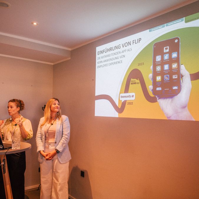 Two people presenting a slide titled Einführung von Flip with a mobile app image.