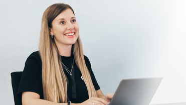 Smiling woman at desk with laptop, representing positive Employee Experience Platform and HR-Software.