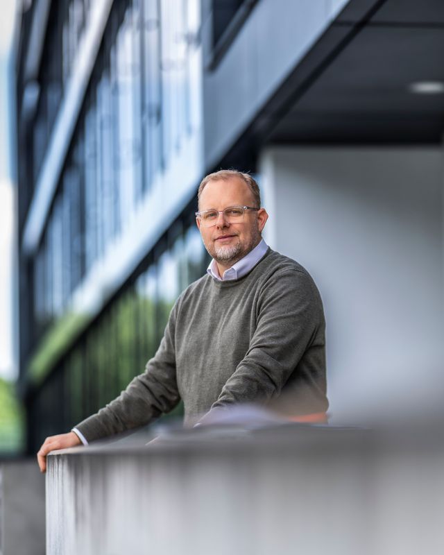 Man in a sweater standing outside a modern building.