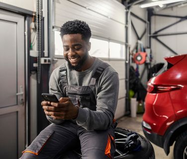 Smiling mechanic using smartphone in garage.