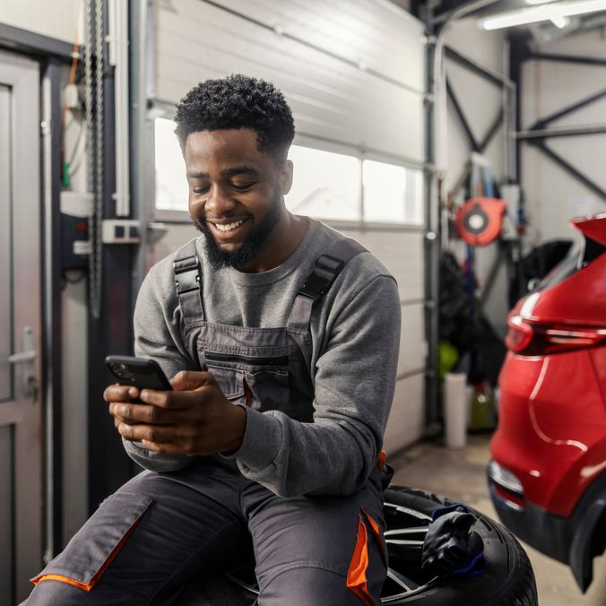 Smiling mechanic using smartphone in garage.
