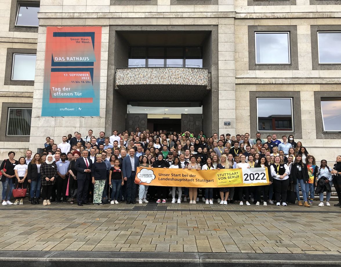 Large group of trainees in front of Stuttgart Rathaus holding a banner: Unser Start bei der Landeshauptstadt Stuttgart 2022.