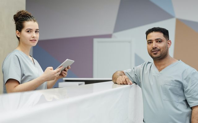 Two nurses in scrubs at a hospital reception, one holding a tablet, modern surgery environment.