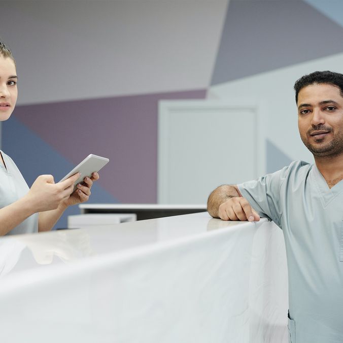 Two nurses in scrubs at a hospital reception, one holding a tablet, modern surgery environment.