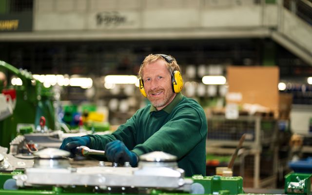 A worker with earmuffs smiling in a factory setting.