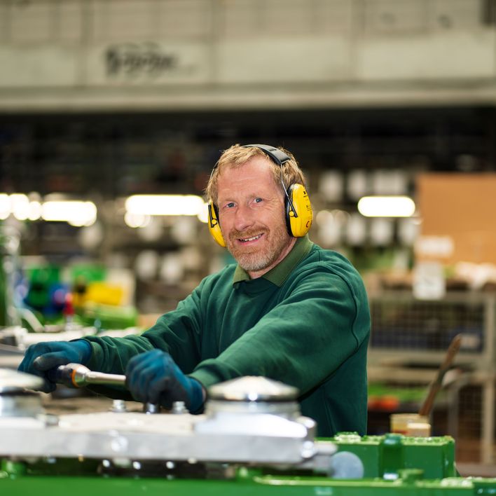 A worker with earmuffs smiling in a factory setting.