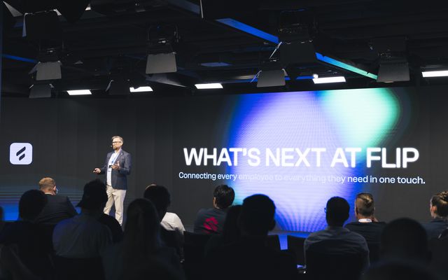 A speaker at a Flip event with text WHATS NEXT AT FLIP on screen.
