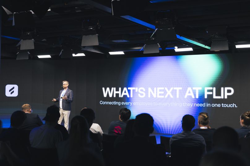 A speaker at a Flip event with text WHATS NEXT AT FLIP on screen.