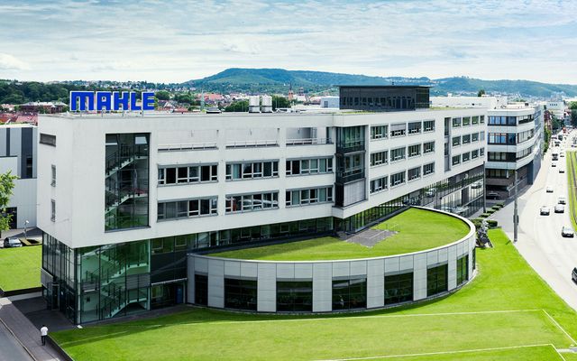 Modern Mahle headquarters building with glass facade, green lawn, and cityscape in the background.