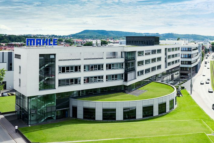 Modern Mahle headquarters building with glass facade, green lawn, and cityscape in the background.