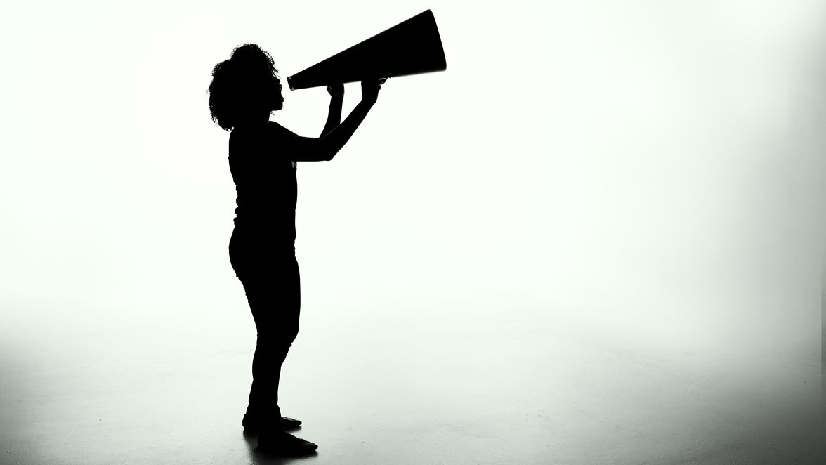 Silhouette of a person using a megaphone in a bright, empty space.