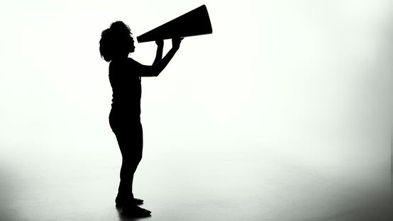 Silhouette of a person using a megaphone in a bright, empty studio environment.