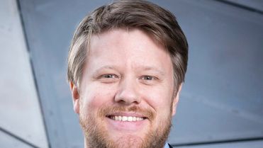 Smiling person in a suit with a geometric background.