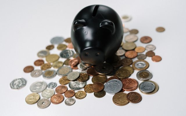 Black piggy bank surrounded by assorted coins on a white surface, symbolizing saving money.