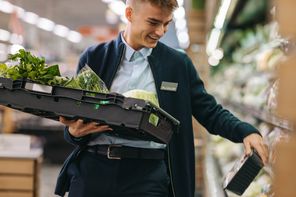 A person in a store holding a crate of fresh greens, smiling.