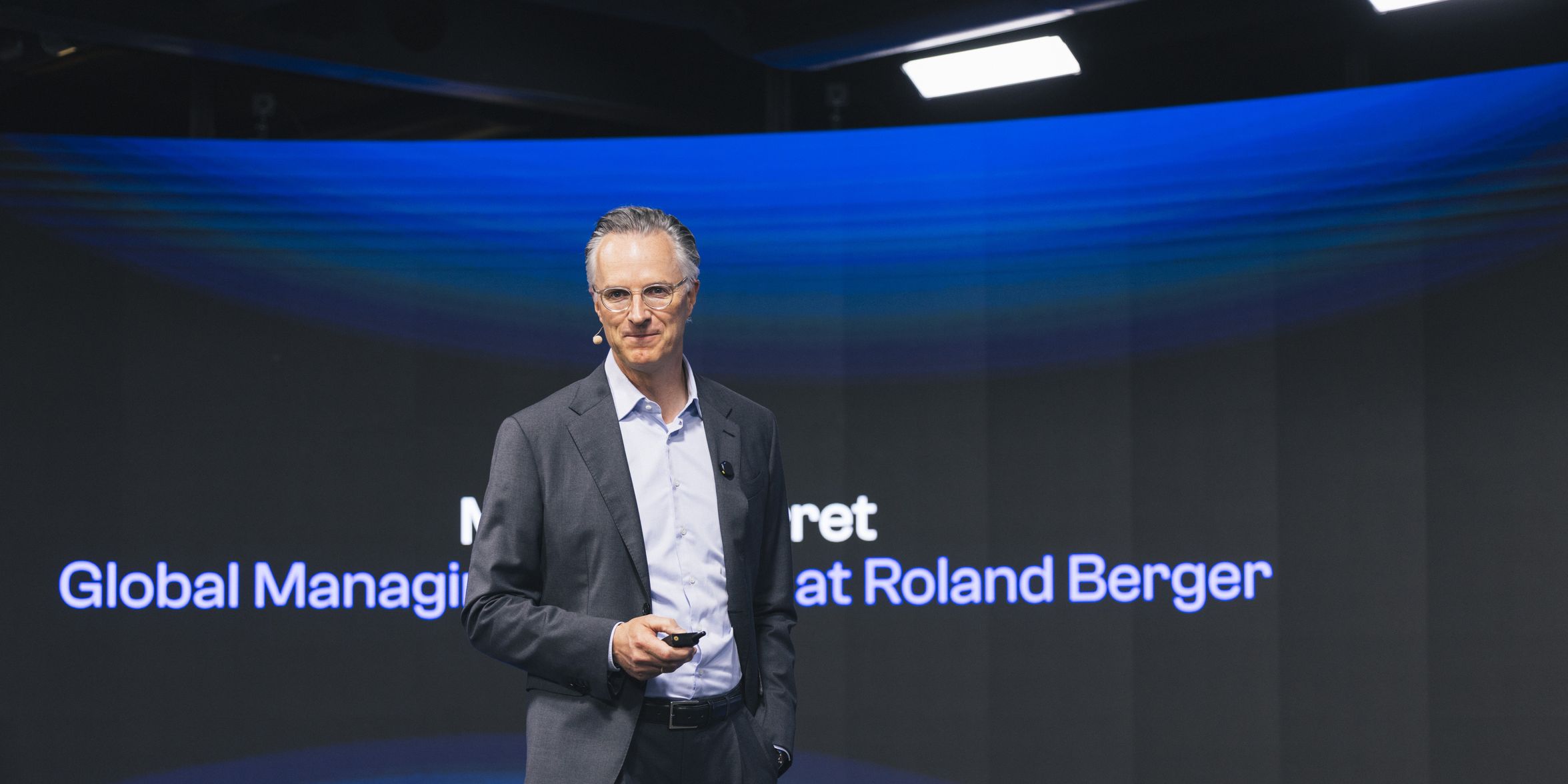 Person on stage with text: Global Managing at Roland Berger.