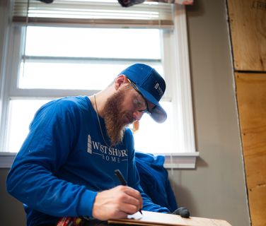 A worker in West Shore Home attire taking notes indoors.