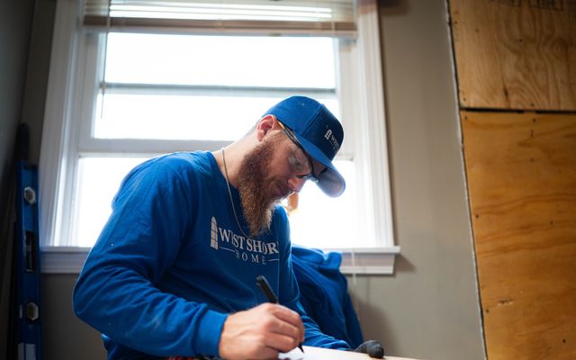 A worker in West Shore Home attire taking notes indoors.