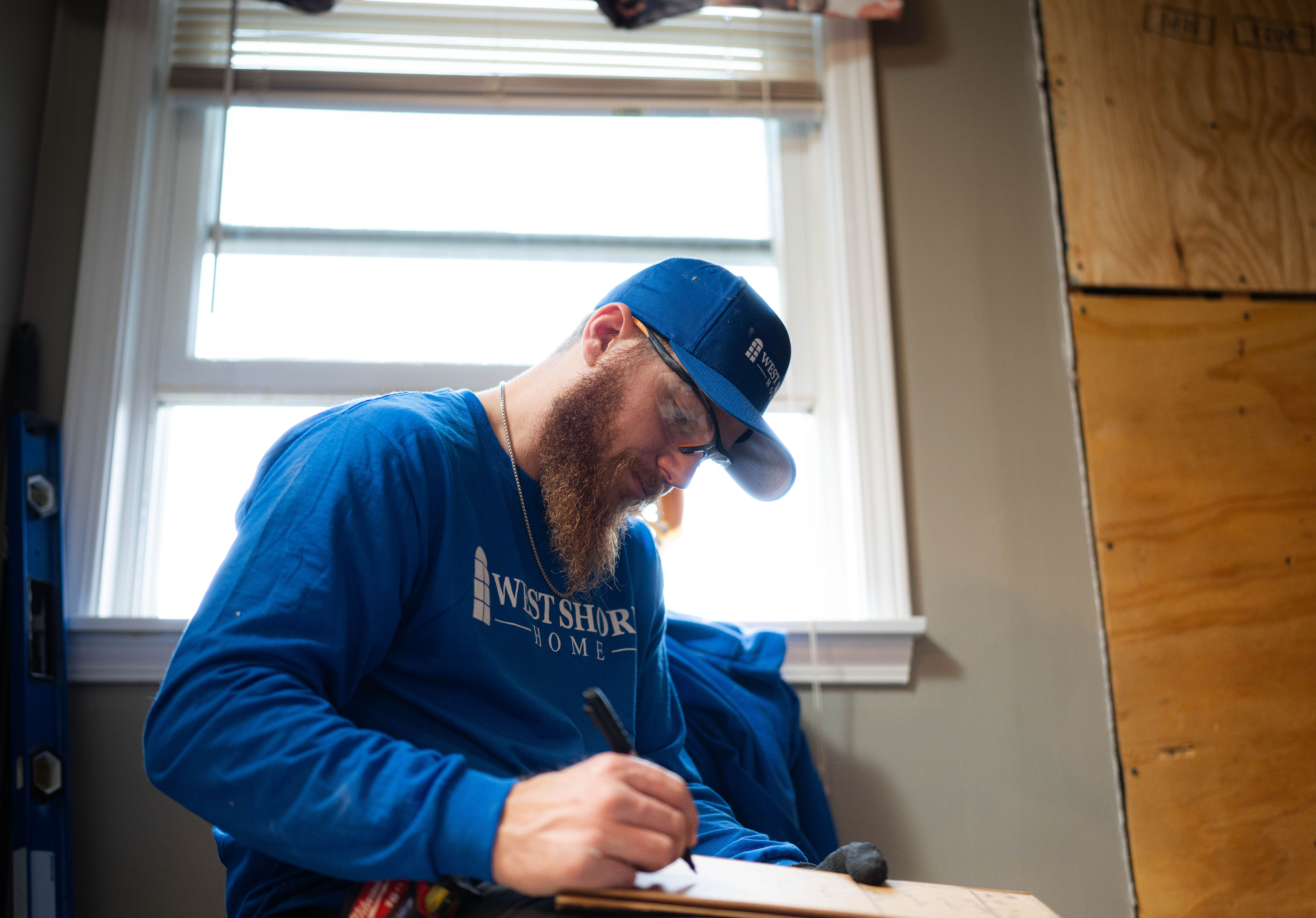 A worker in West Shore Home attire taking notes indoors.