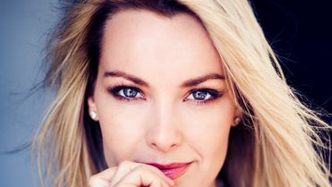 Portrait of a woman with blonde hair, wearing a black top, looking confidently at the camera.