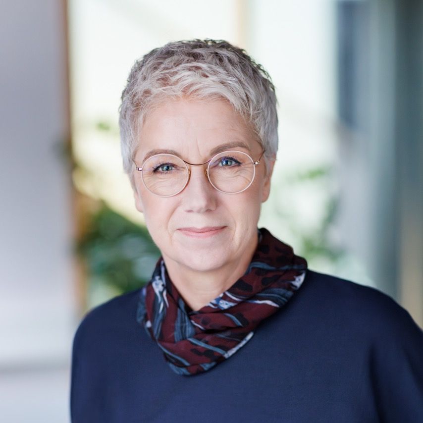 Portrait of an older woman with short gray hair and glasses, wearing a dark top and scarf.