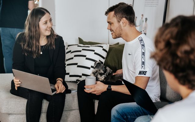 People chatting on a couch with laptops and a dog.