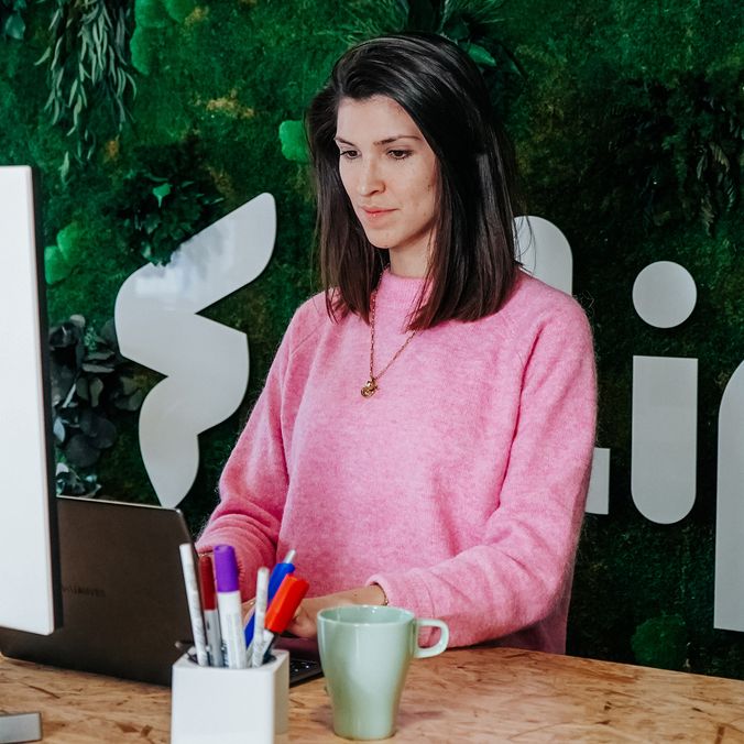 Woman at standing desk in modern office, green wall, Flip Mitarbeiterplattform branding visible.