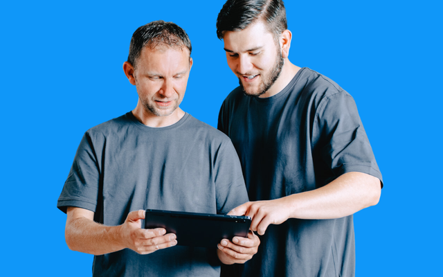 Two men in grey shirts use a tablet, symbolizing Employee App, Mitarbeiterplattform, HR-Software.