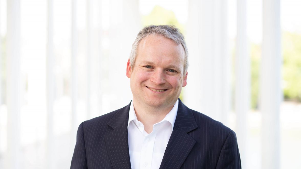 Smiling person in a suit with a bright, blurred background.