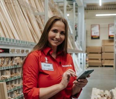 Mitarbeiterin im toom-Markt nutzt Smartphone; Mitarbeiter App, Employee Experience Platform sichtbar.